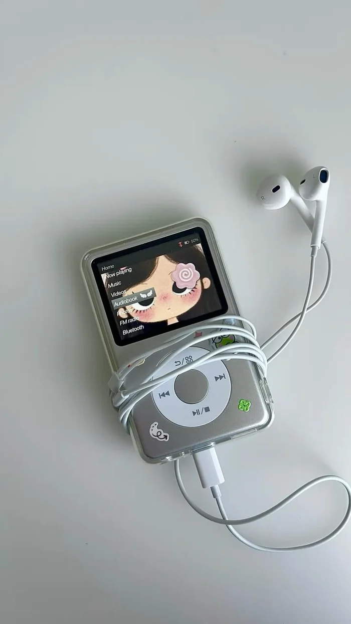 A silver MP3 player with a clear case and stickers, wrapped in white wired earbuds